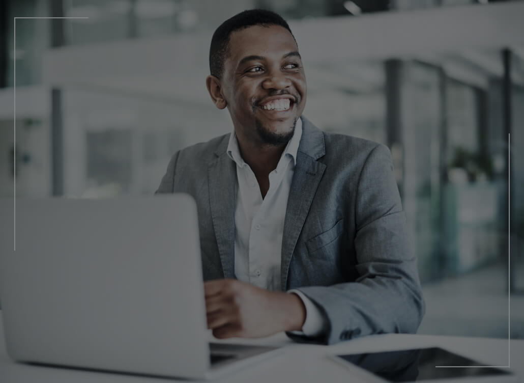 A man in a suit smiles as he sits in front of a laptop. A man in a suit smiles as he sits in front of a laptop.